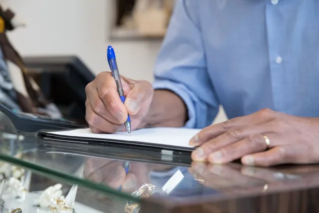 A person writing in a notebook at a glass counter, capturing business and office themes. How Much Does a Pennsylvania Birth Certificate Cost for Heritage Research?