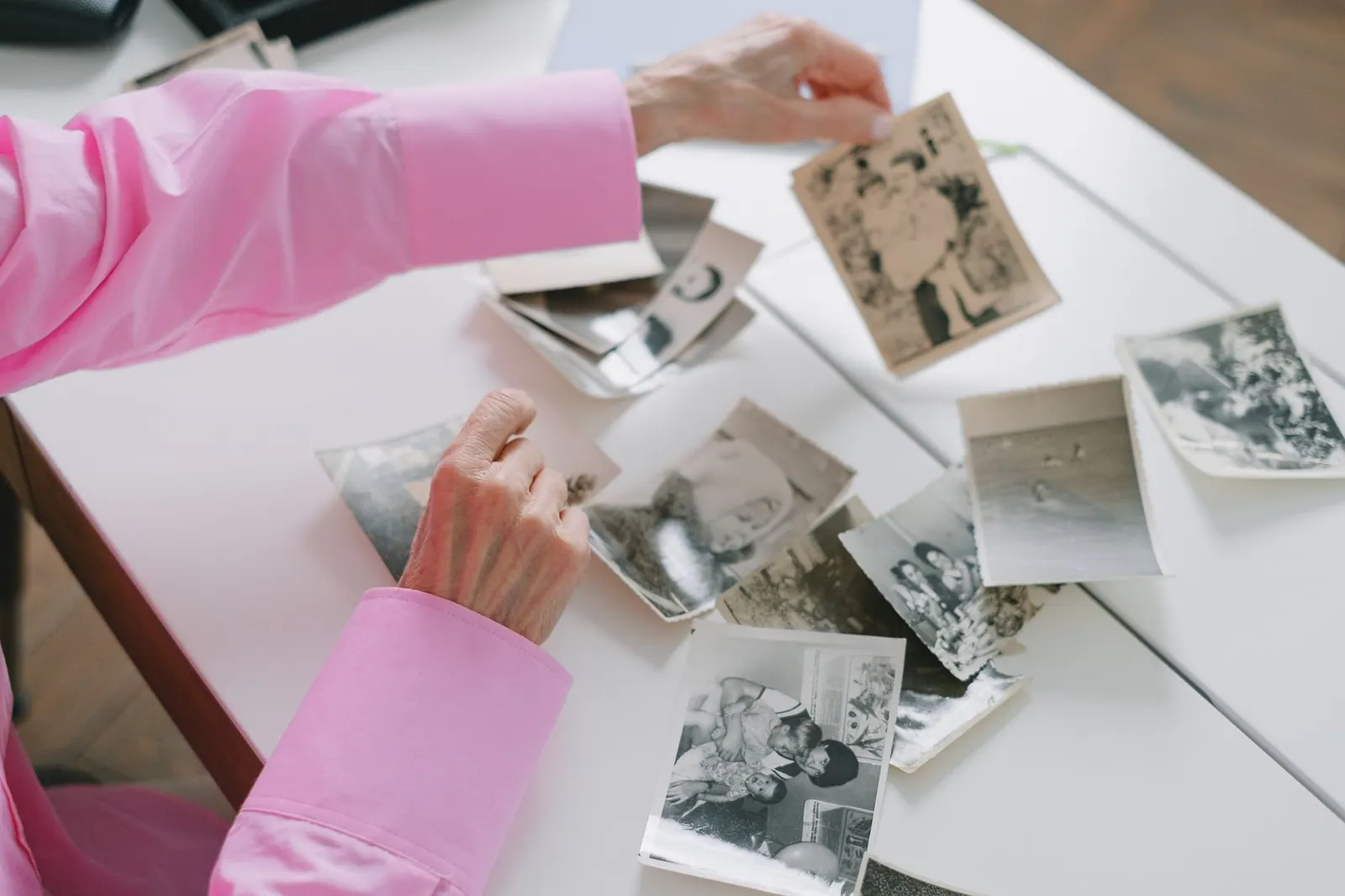 An elderly woman in a pink shirt sorting through old black and white family photographs, evoking nostalgia. People by heritage list: a researched guide